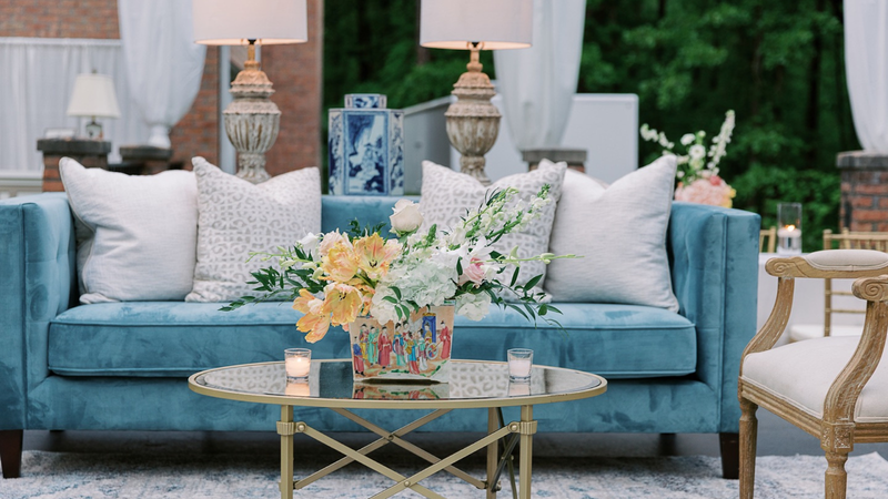 Floral centerpiece on golden coffee table, near blue plush sofa by EventWorks