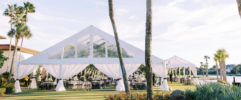 A large white tent set up outdoors on a sunny day for a beautiful wedding reception.