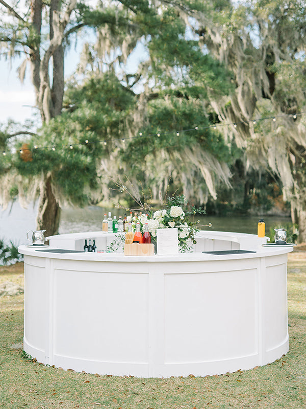 A circular bar set up outdoors at the edge of a pond. Flowers are in the center.