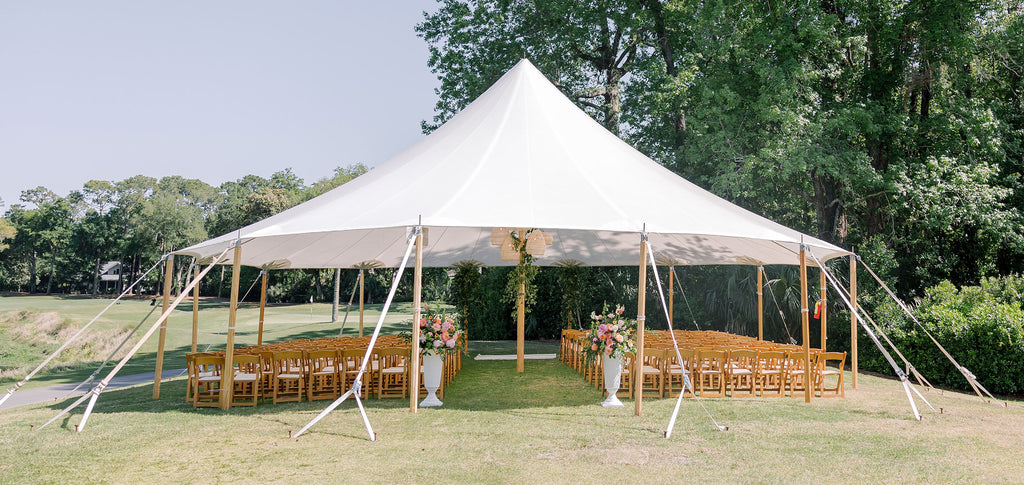 A beautiful rental tent set up for a wedding with wood folding chairs for an audience.
